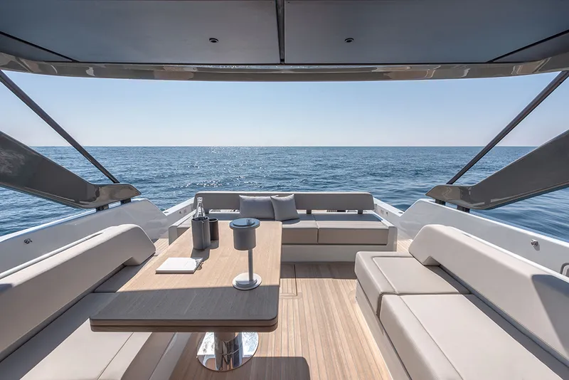 Solarium of a new yacht in Mallorca. Spacious sofa in beige and teak surface floor. Big wood table in the middle.
