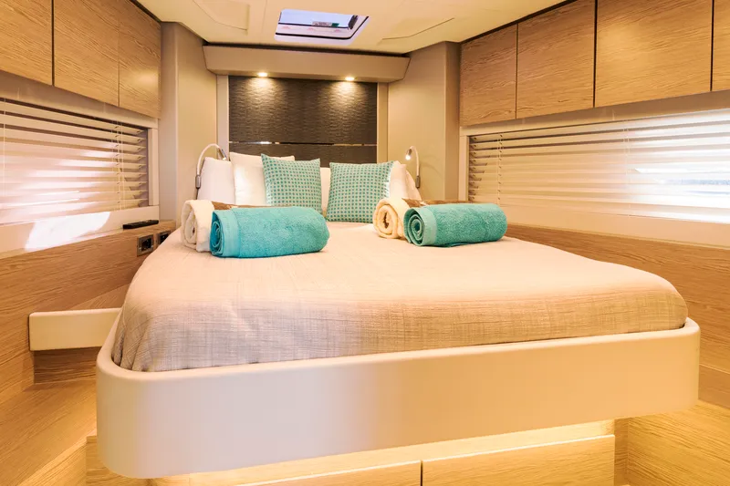 Yacht cabin in Mallorca. Big spacious bed with beige bed linen. Lights are on.