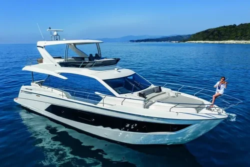 yacht in charter in Mallorca anchored at a bay. New boat from 2023 has a spacious flybridge. Beige sofa area. Sunny day.
